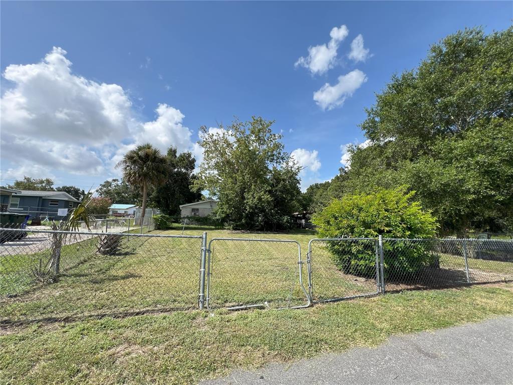 A chain-link fence encloses a grassy vacant lot with trees under a blue sky — 510 PICKENS STREET, LAKELAND, FL