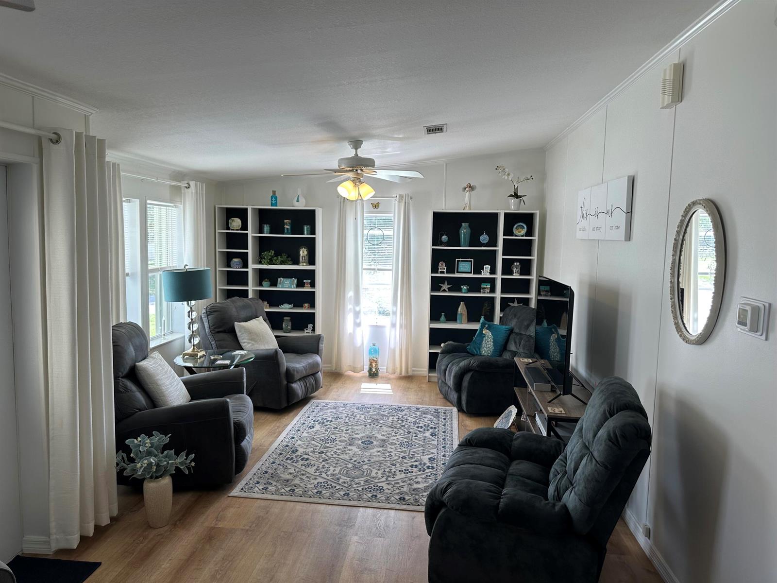 A living room features dark gray recliners, white bookshelves, a patterned area rug, and wood-look flooring — 500 Thames Bluff Ridge # 24, Fort Pierce FL 34982, FORT PIERCE, FL