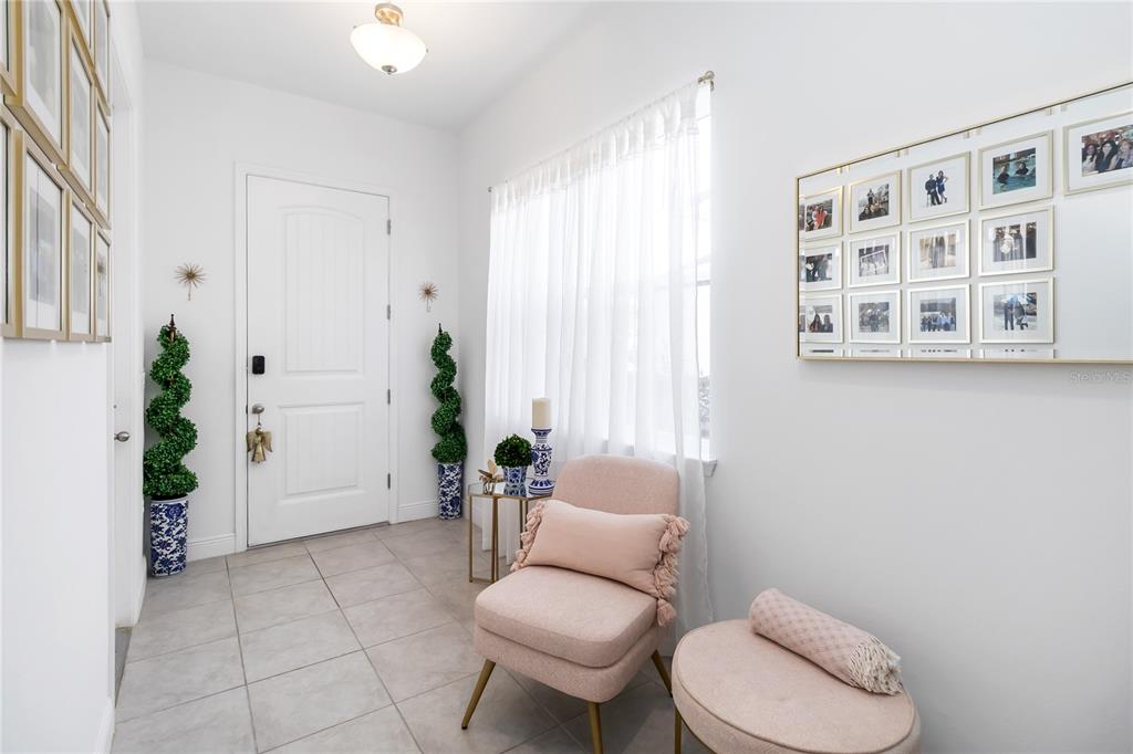 A bright entryway features tile flooring, a pink armchair, a matching ottoman, and wall-mounted photos — 15742 VETTA DRIVE, MONTVERDE, FL