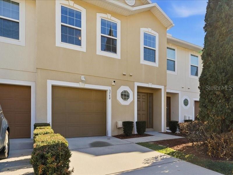 A two-story tan townhouse with a garage and a small front garden — 3740 WOODBURY HILL LOOP, LAKELAND, FL