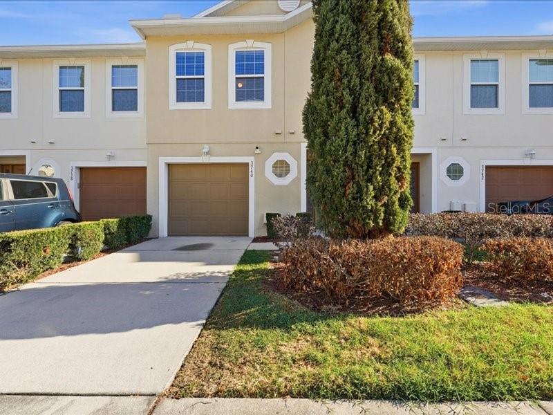 A two-story townhouse exterior with a single-car garage, beige siding, and a small front lawn — 3740 WOODBURY HILL LOOP, LAKELAND, FL