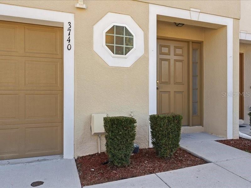 The exterior of a tan townhouse features a garage, a front door, and two bushes — 3740 WOODBURY HILL LOOP, LAKELAND, FL