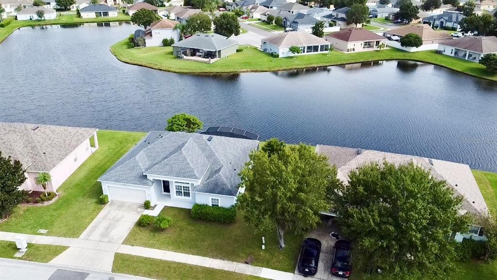 An aerial view shows a suburban neighborhood with houses surrounding a central lake — 3807 WOOD THRUSH DRIVE, KISSIMMEE, FL