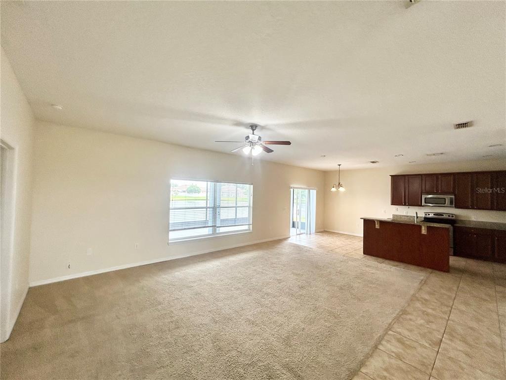 A living room with beige carpet opens to a kitchen with dark wood cabinets — 3807 WOOD THRUSH DRIVE, KISSIMMEE, FL
