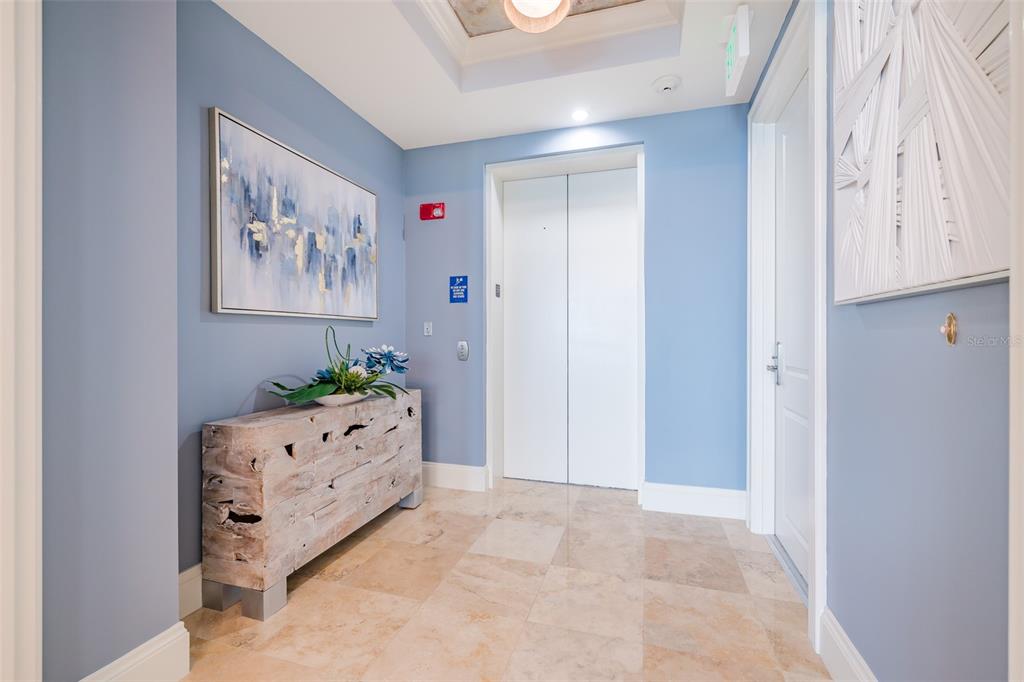 A hallway features blue walls, a rustic wooden console table, and a white elevator door — 130 RIVIERA DUNES WAY UNIT 802, PALMETTO, FL