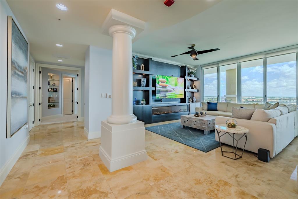 A living room features a white column, tile flooring, a large sectional, and a media wall — 130 RIVIERA DUNES WAY UNIT 802, PALMETTO, FL