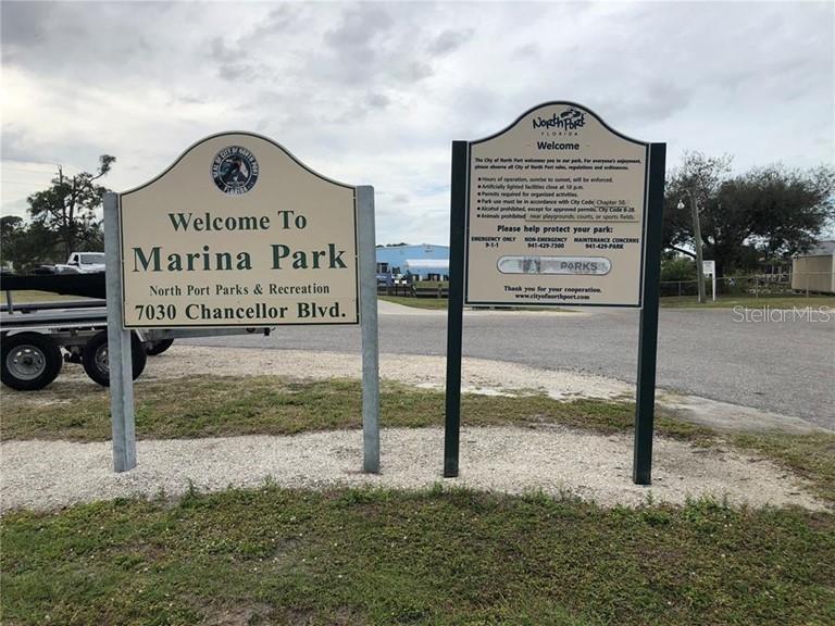 Two signs stand at the entrance to a park with a gravel parking area — CHANNING AVENUE, NORTH PORT, FL