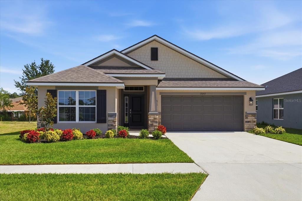 A single-story suburban house features a two-car garage, stone accents, and a landscaped front yard — 13243 OGDEN GLADE ROAD, DADE CITY, FL