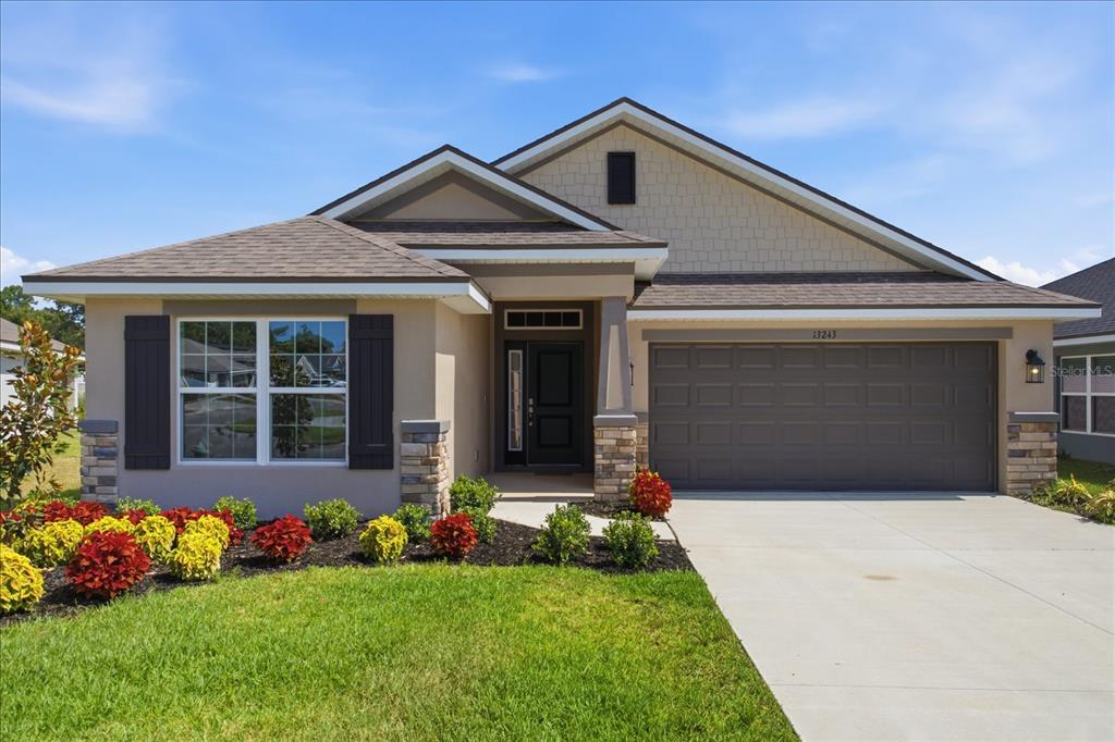 A single-story house with a tan stucco exterior, stone accents, and a two-car garage — 13243 OGDEN GLADE ROAD, DADE CITY, FL