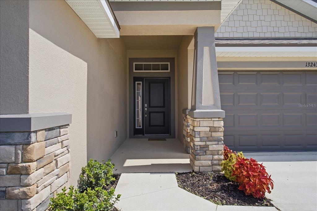 The exterior of a house features a stone-accented entryway, a dark front door, and garage — 13243 OGDEN GLADE ROAD, DADE CITY, FL