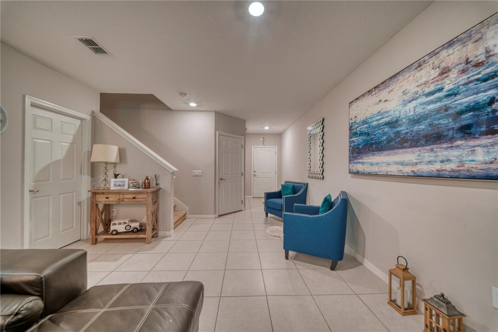 A tiled entryway features a staircase, two blue armchairs, and a large abstract wall painting — 3390 BELLEZZA COURT, KISSIMMEE, FL