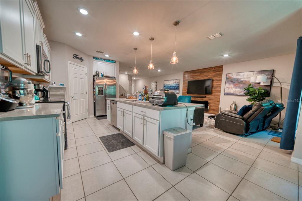 A kitchen with white cabinets and a central island opens into a living room area — 3390 BELLEZZA COURT, KISSIMMEE, FL