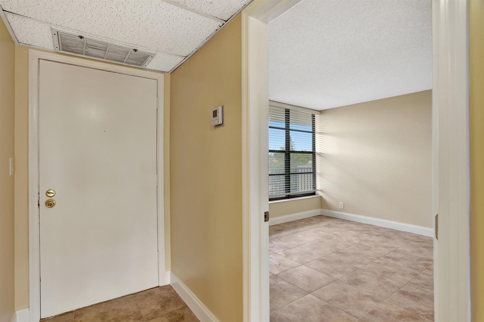 A view from a tiled hallway into an empty room with large windows and blinds — 3 Royal Palm Way Unit 403, Boca Raton FL 33432, BOCA RATON, FL