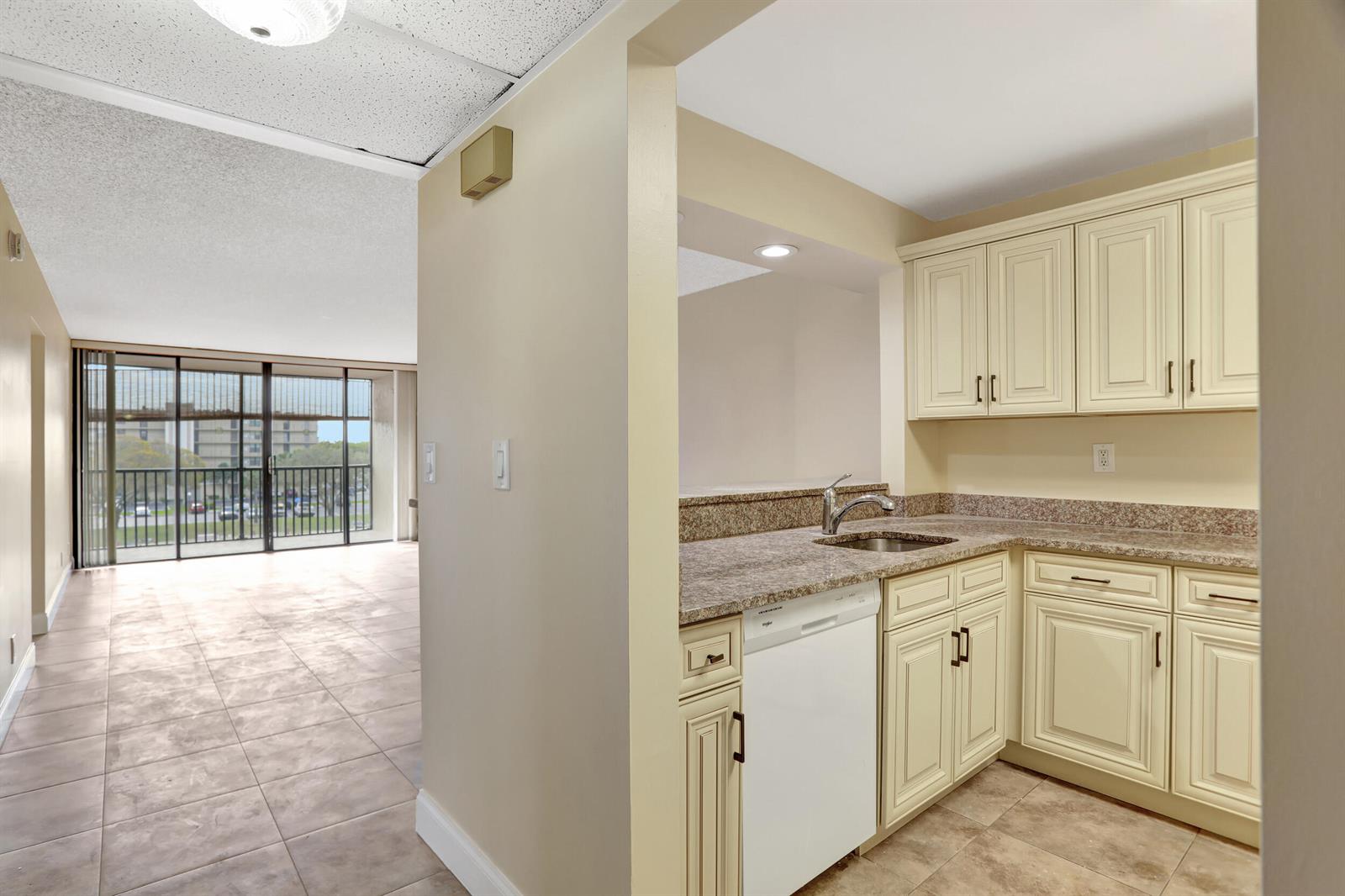 A kitchen with cream cabinets and granite countertops opens to a living area with balcony access — 3 Royal Palm Way Unit 403, Boca Raton FL 33432, BOCA RATON, FL