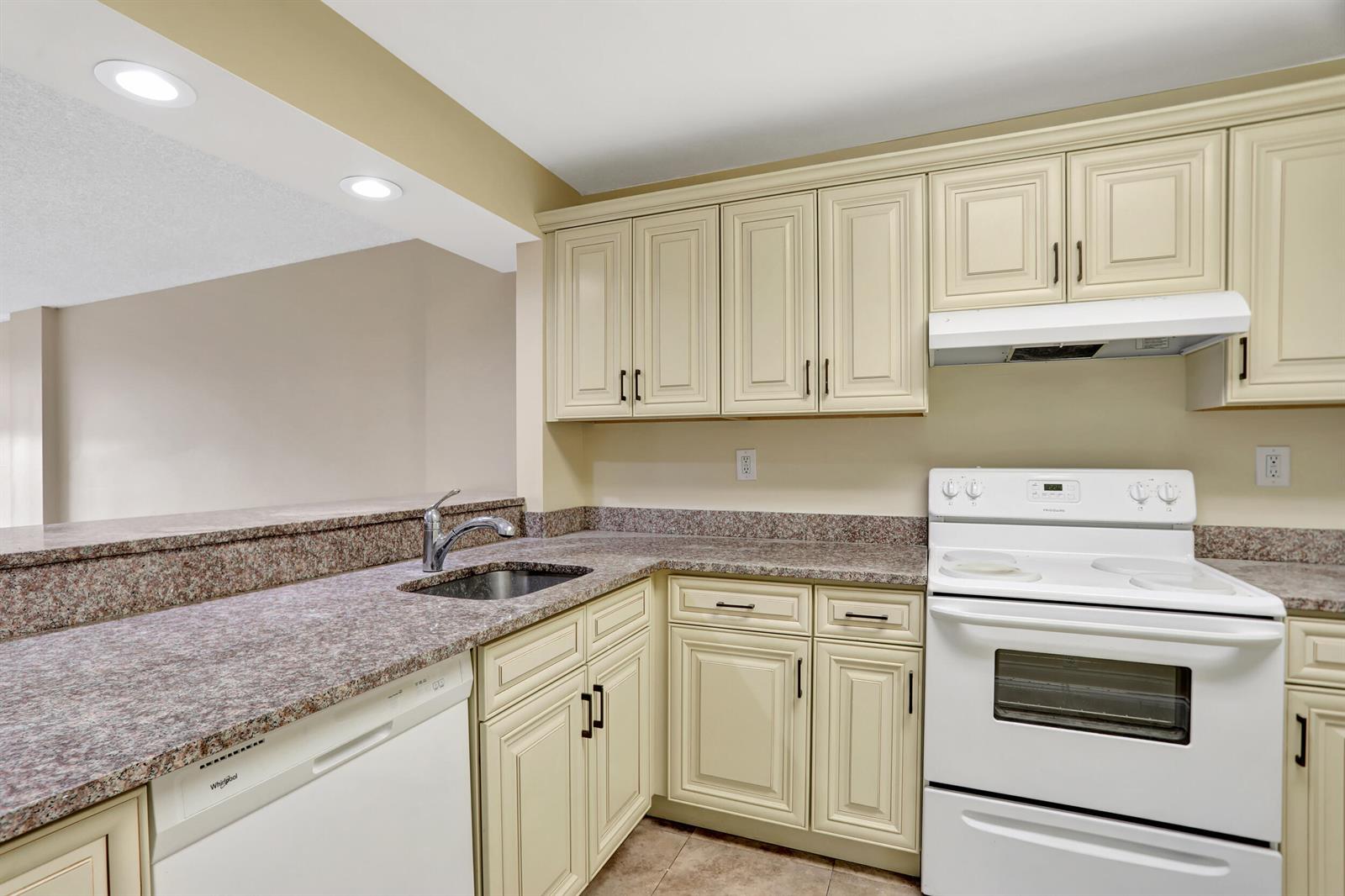 A kitchen features cream-colored cabinets, granite countertops, a white stove, and a stainless steel sink — 3 Royal Palm Way Unit 403, Boca Raton FL 33432, BOCA RATON, FL