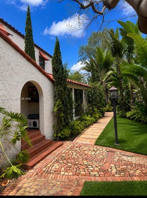 A lush backyard features a brick walkway, a large leaning tree, and a wooden pergola — 8276 E Dixie Hwy, Miami FL 33138, MIAMI, FL