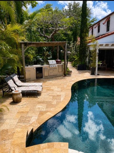 A backyard features a stone patio, a green lawn, lush tropical plants, and a pergola — 8276 E Dixie Hwy, Miami FL 33138, MIAMI, FL