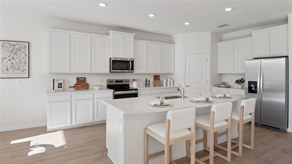 A modern kitchen features white cabinetry, stainless steel appliances, a center island, and light flooring — 12728 NW 17TH PLACE, NEWBERRY, FL
