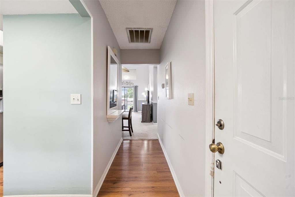 A hallway with wood-look flooring leads from a white door toward an open living area — 2600 LUCERNE PARK ROAD UNIT 521, WINTER HAVEN, FL