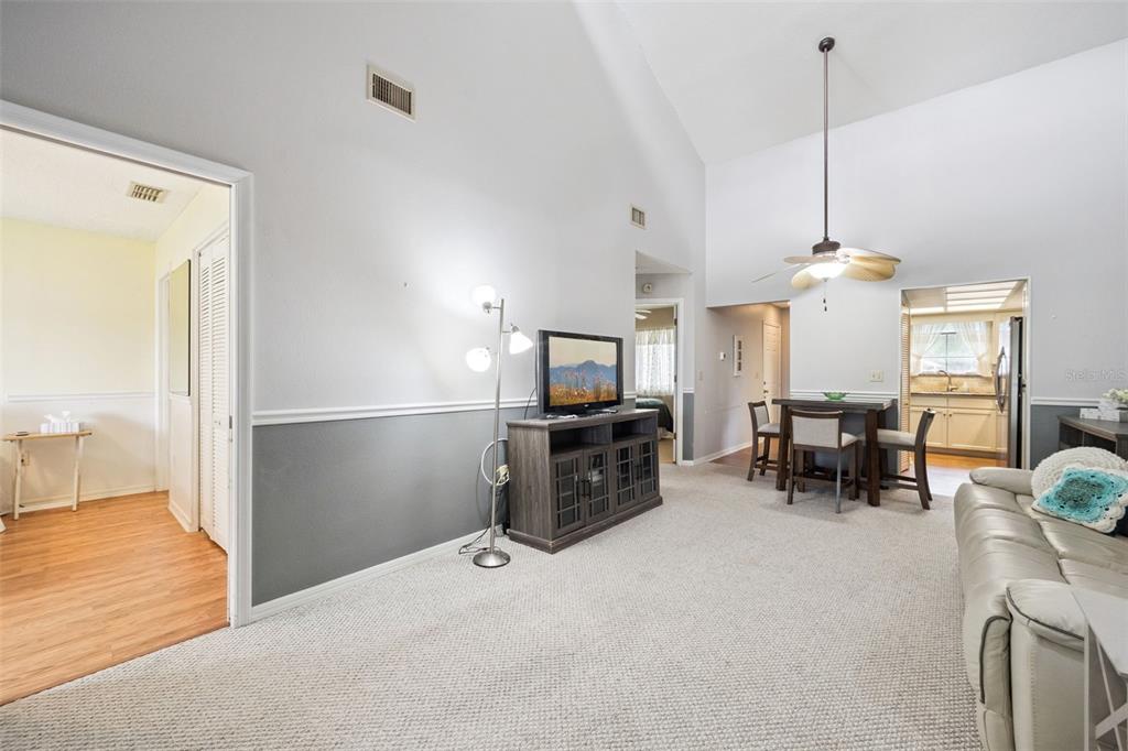 A living room features vaulted ceilings, gray and white walls, carpeted floors, and a dining area — 2600 LUCERNE PARK ROAD UNIT 521, WINTER HAVEN, FL