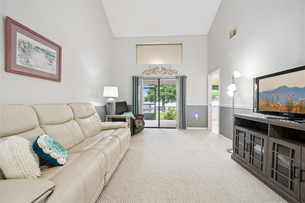 A living room features a vaulted ceiling, light-colored carpet, a leather sofa, and sliding doors — 2600 LUCERNE PARK ROAD UNIT 521, WINTER HAVEN, FL