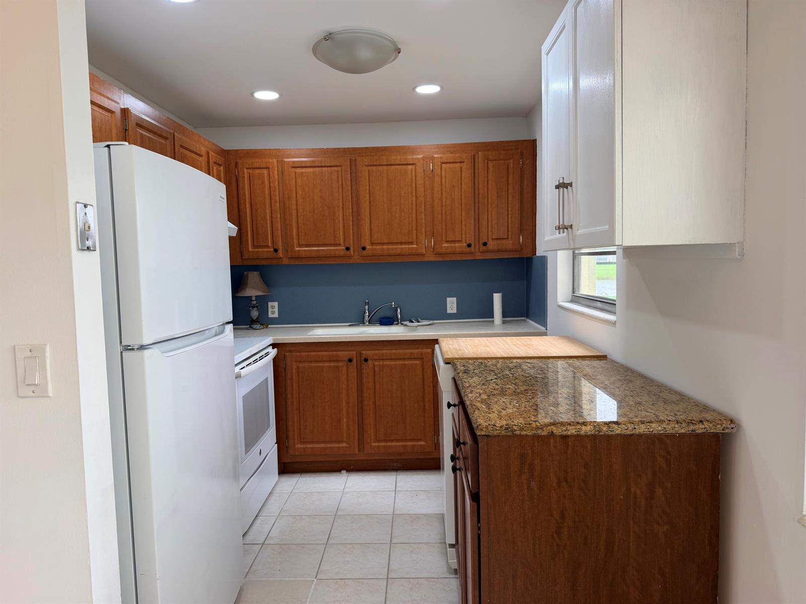 A kitchen features wood cabinets, granite countertops, a white refrigerator, and a blue backsplash — 52 Dorset Drive # B, Boca Raton FL 33434, BOCA RATON, FL