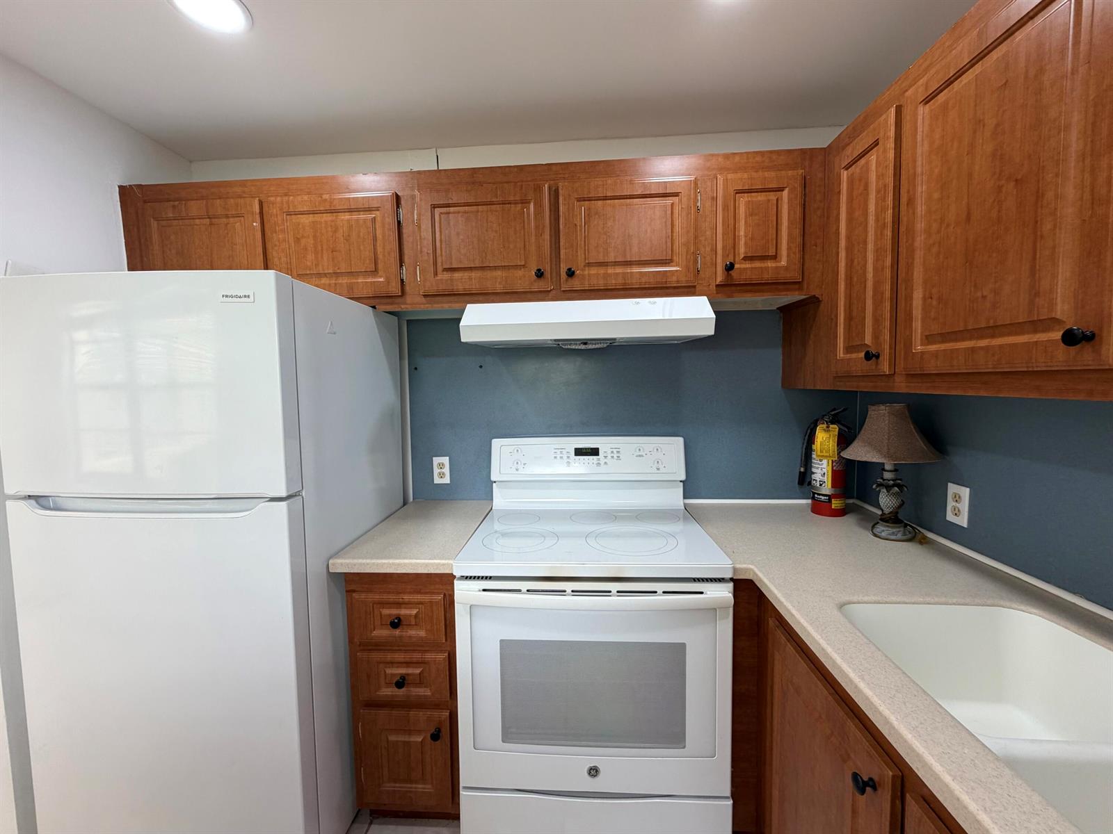 A kitchen features wood cabinets, white appliances, a blue backsplash, and a beige countertop — 52 Dorset Drive # B, Boca Raton FL 33434, BOCA RATON, FL
