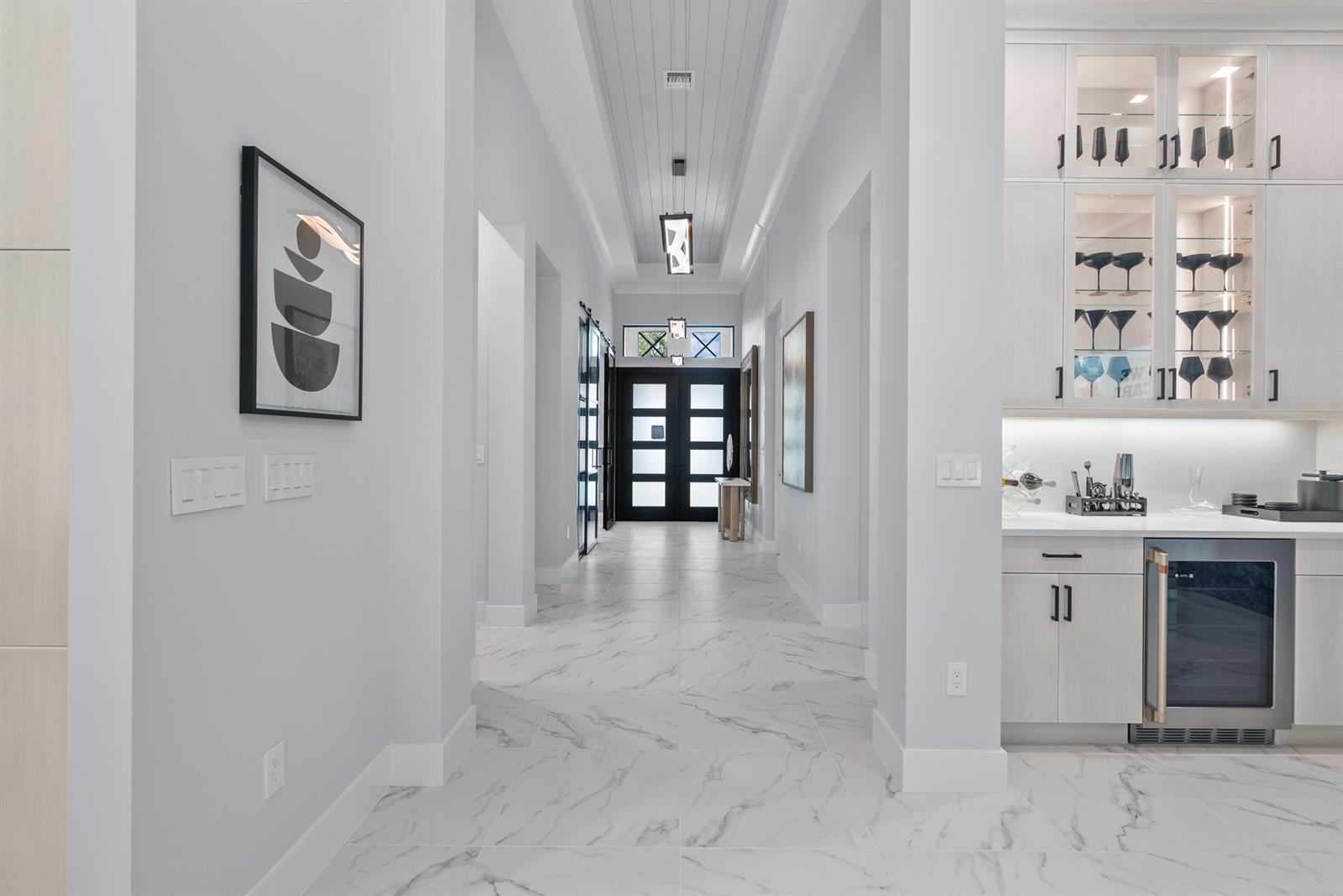 A hallway with marble-look tile flooring leads to a dark-framed front door with glass panels — 9259 Seaglass Court, Vero Beach FL 32963, VERO BEACH, FL