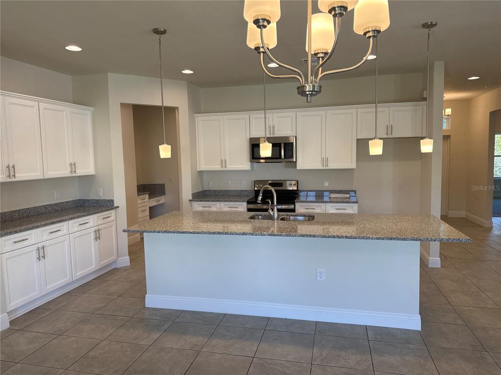 A kitchen features white cabinets, granite countertops, a central island, and stainless steel appliances — 5372 JODY AVENUE, NORTH PORT, FL