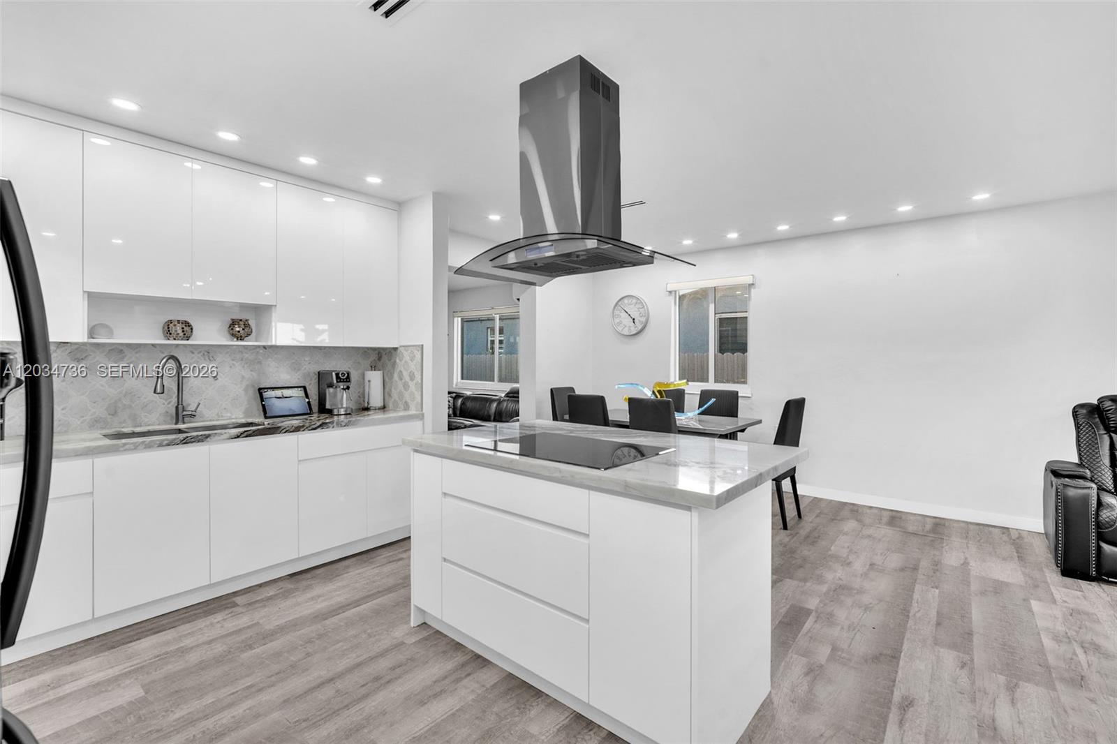 A modern kitchen features white cabinetry, a marble-topped island with a cooktop, and gray flooring — 380 W 30th St, Hialeah FL 33012, HIALEAH, FL