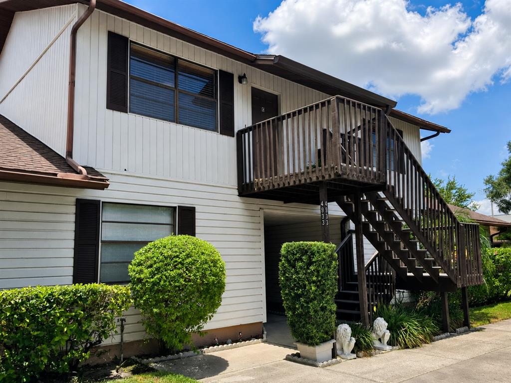A two-story building features white siding, dark shutters, and an exterior wooden staircase — 4933 91ST AVENUE N UNIT 39, PINELLAS PARK, FL