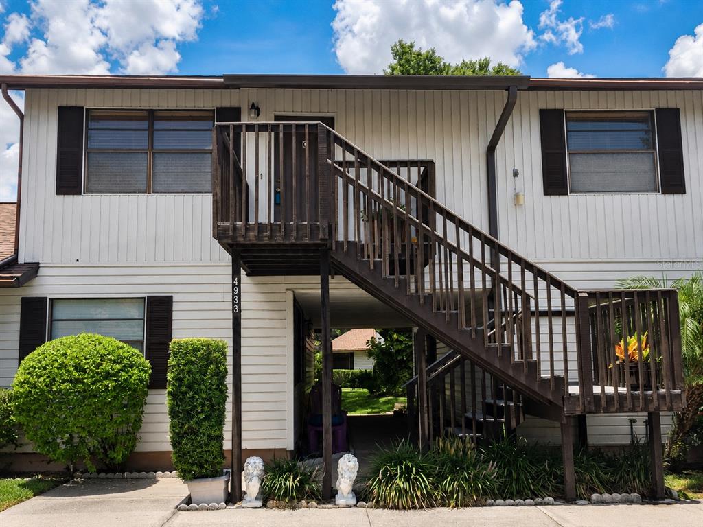 A two-story building exterior features white siding, dark shutters, and an outdoor wooden staircase — 4933 91ST AVENUE N UNIT 39, PINELLAS PARK, FL