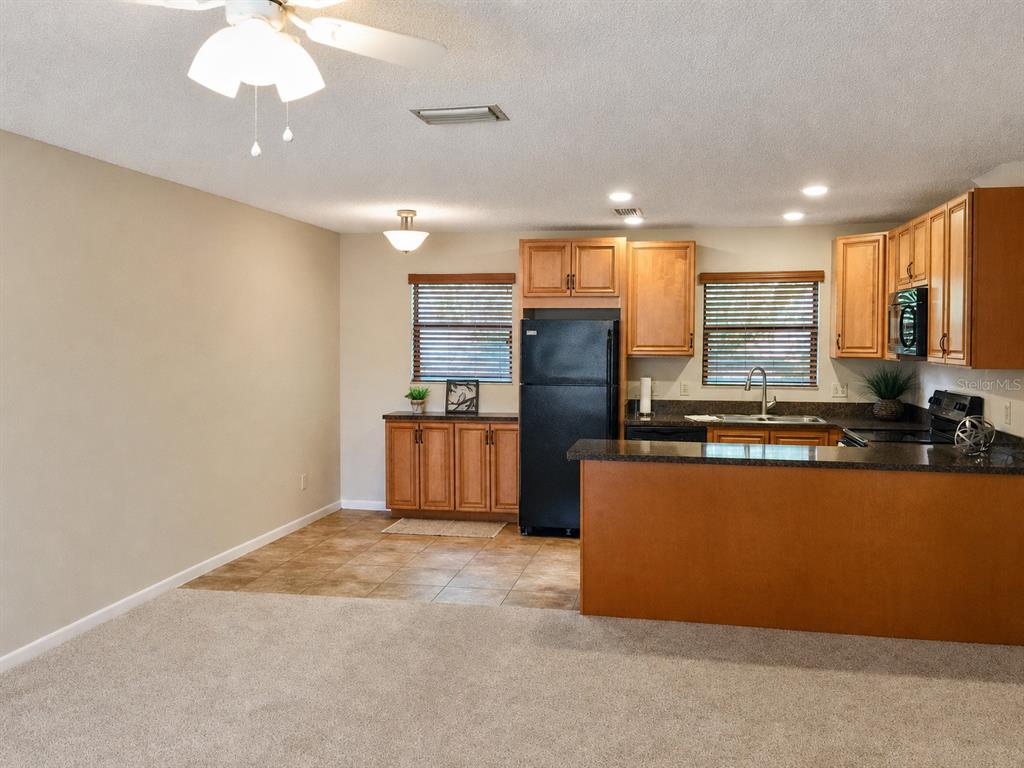 A kitchen with wood cabinets, black appliances, and a breakfast bar overlooks a carpeted area — 4933 91ST AVENUE N UNIT 39, PINELLAS PARK, FL
