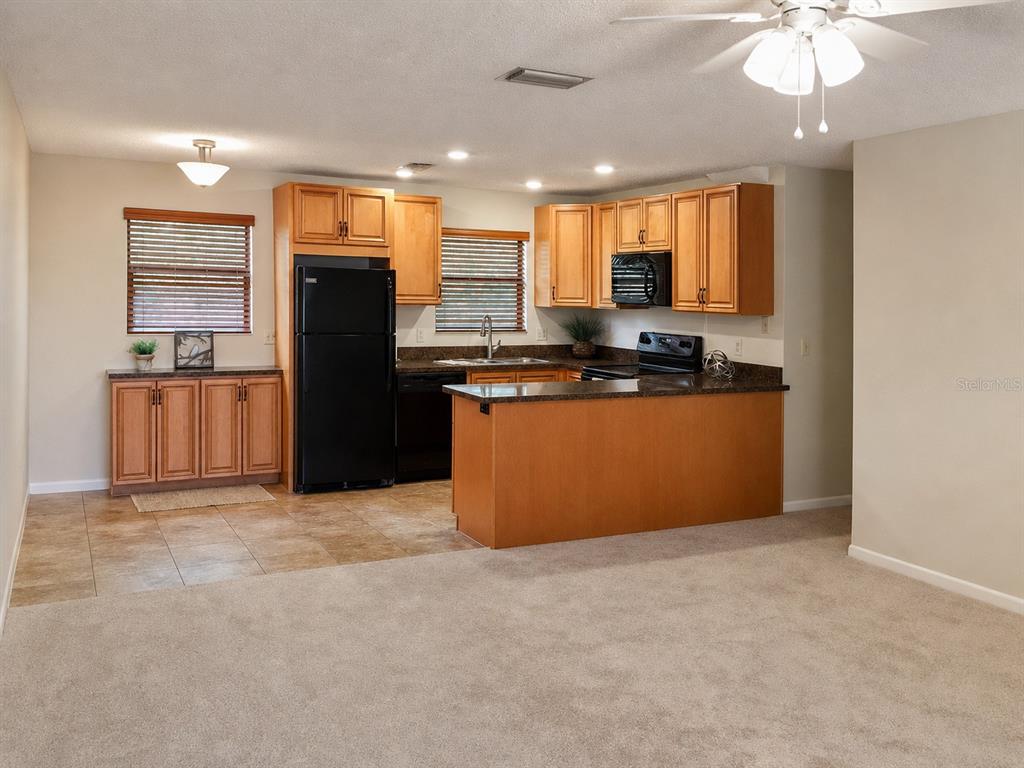 A kitchen features light wood cabinets, black appliances, a peninsula, and tile flooring — 4933 91ST AVENUE N UNIT 39, PINELLAS PARK, FL