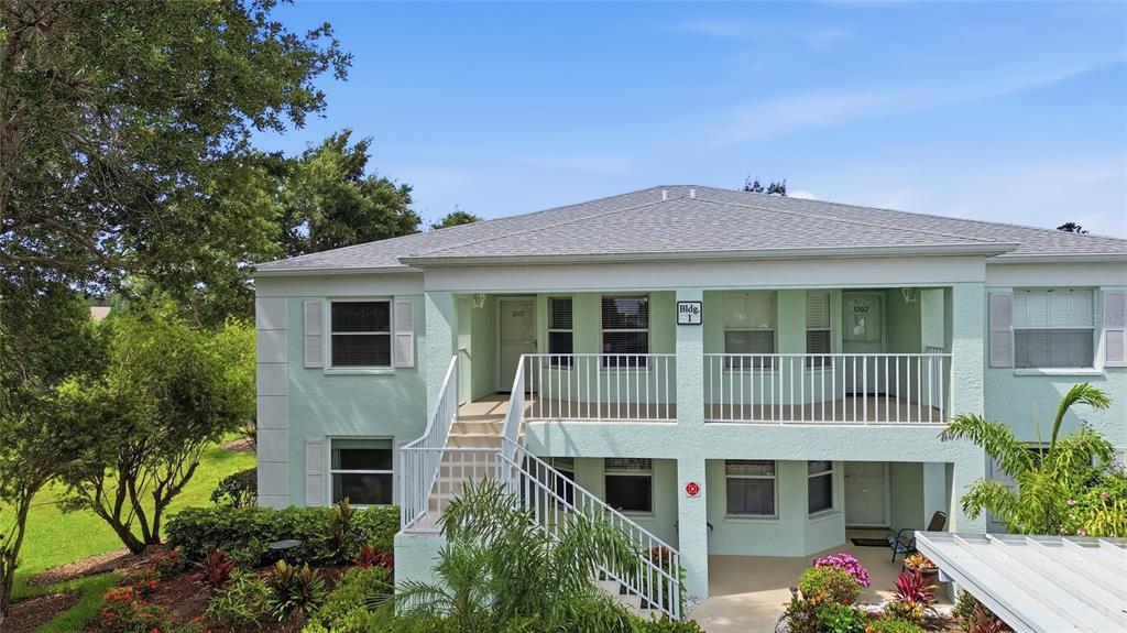 A two-story light green apartment building features a central staircase and a second-floor balcony — 5725 GREENWOOD AVENUE UNIT 1201, NORTH PORT, FL