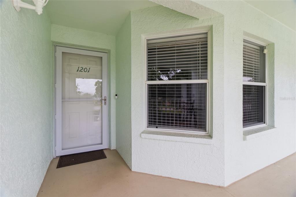 A light green exterior wall features a front door with a storm door and windows — 5725 GREENWOOD AVENUE UNIT 1201, NORTH PORT, FL