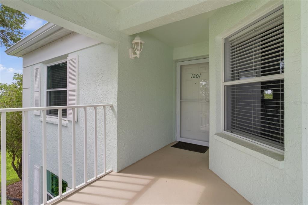 A covered porch leads to a white front door with a storm door and windows — 5725 GREENWOOD AVENUE UNIT 1201, NORTH PORT, FL