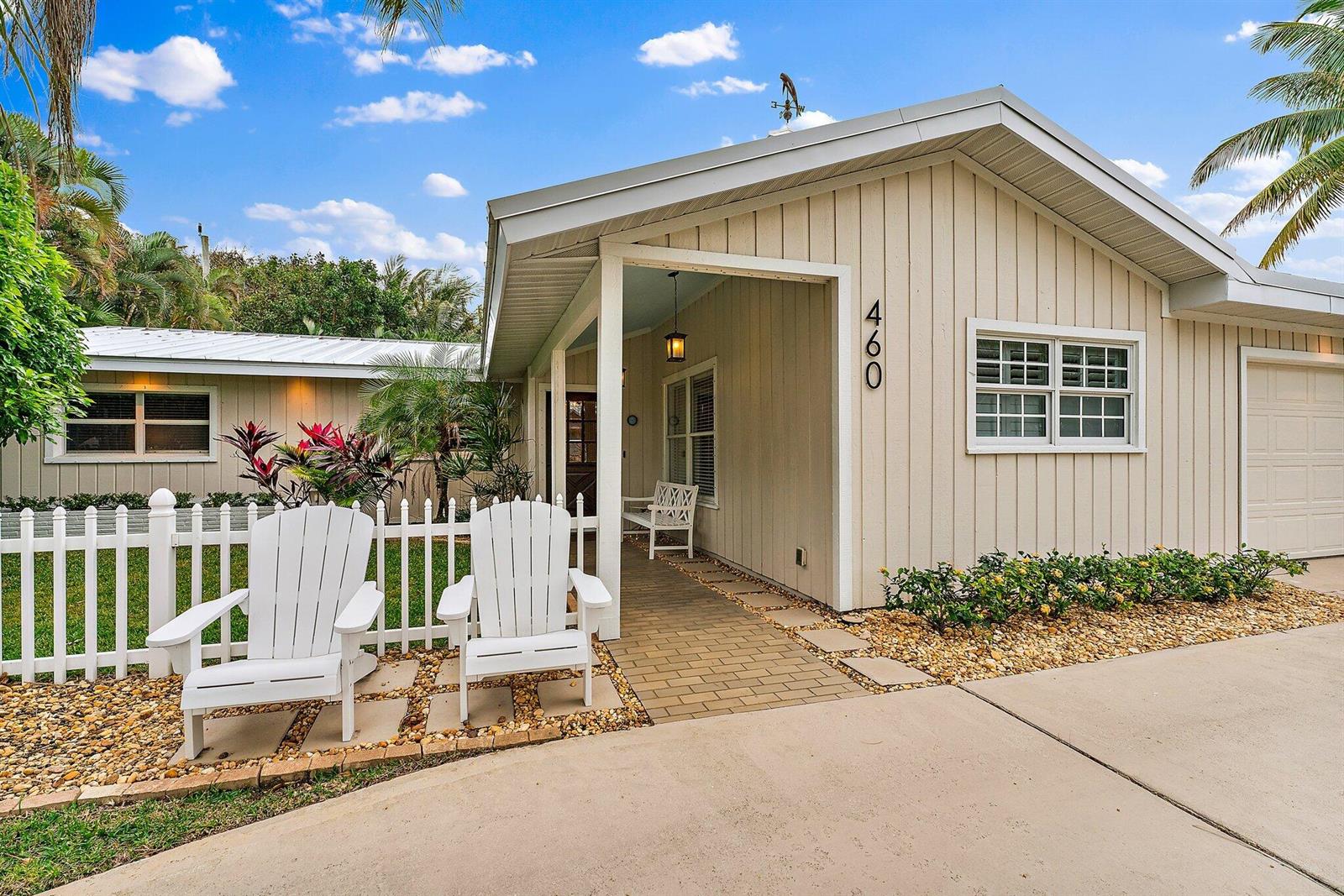 A single-story house with beige vertical siding, a white picket fence, and two white chairs — 460 Sunrise Way, Juno Beach FL 33408, JUNO BEACH, FL