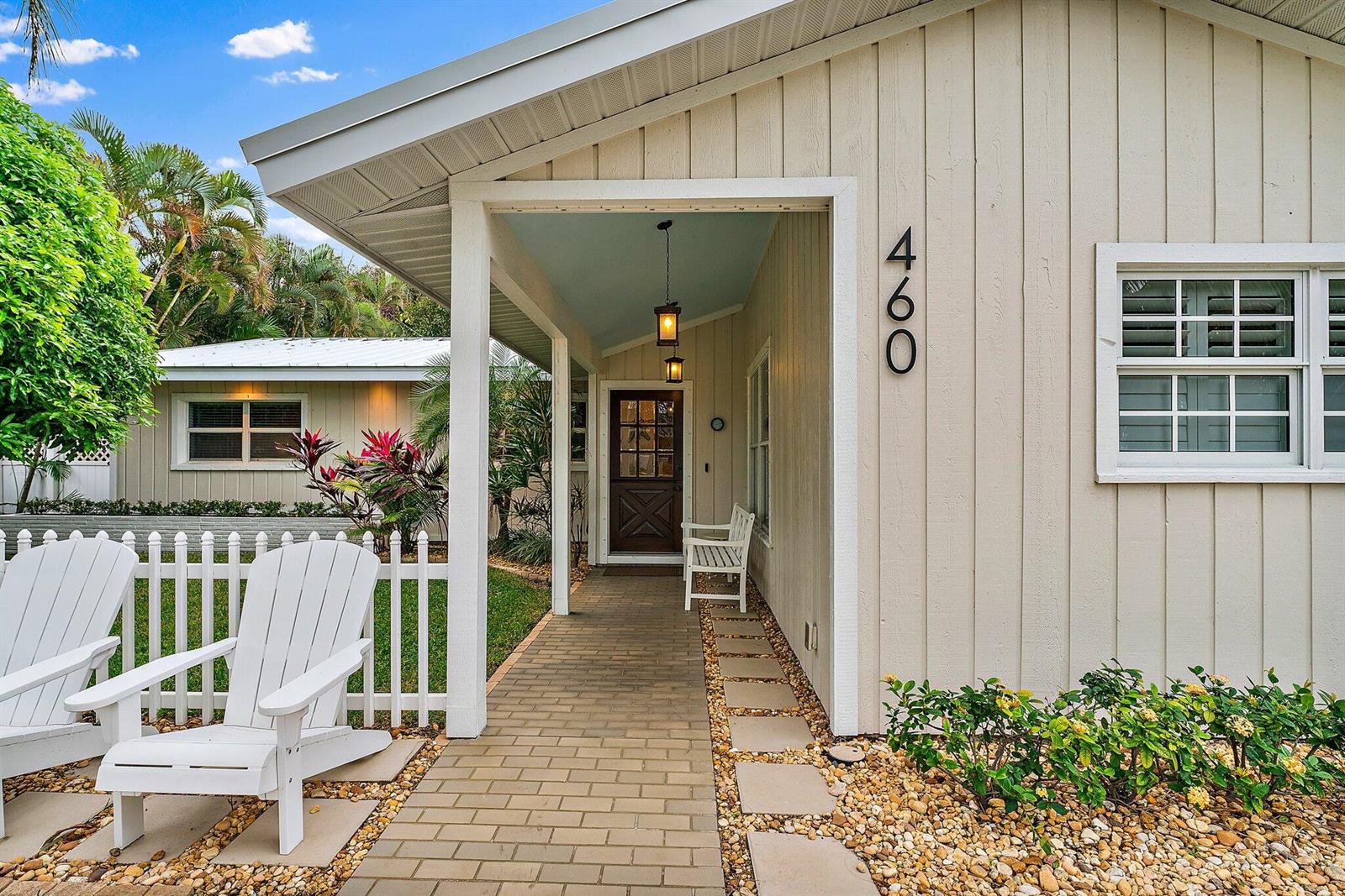 A beige house exterior features a brick walkway, white picket fence, and two Adirondack chairs — 460 Sunrise Way, Juno Beach FL 33408, JUNO BEACH, FL