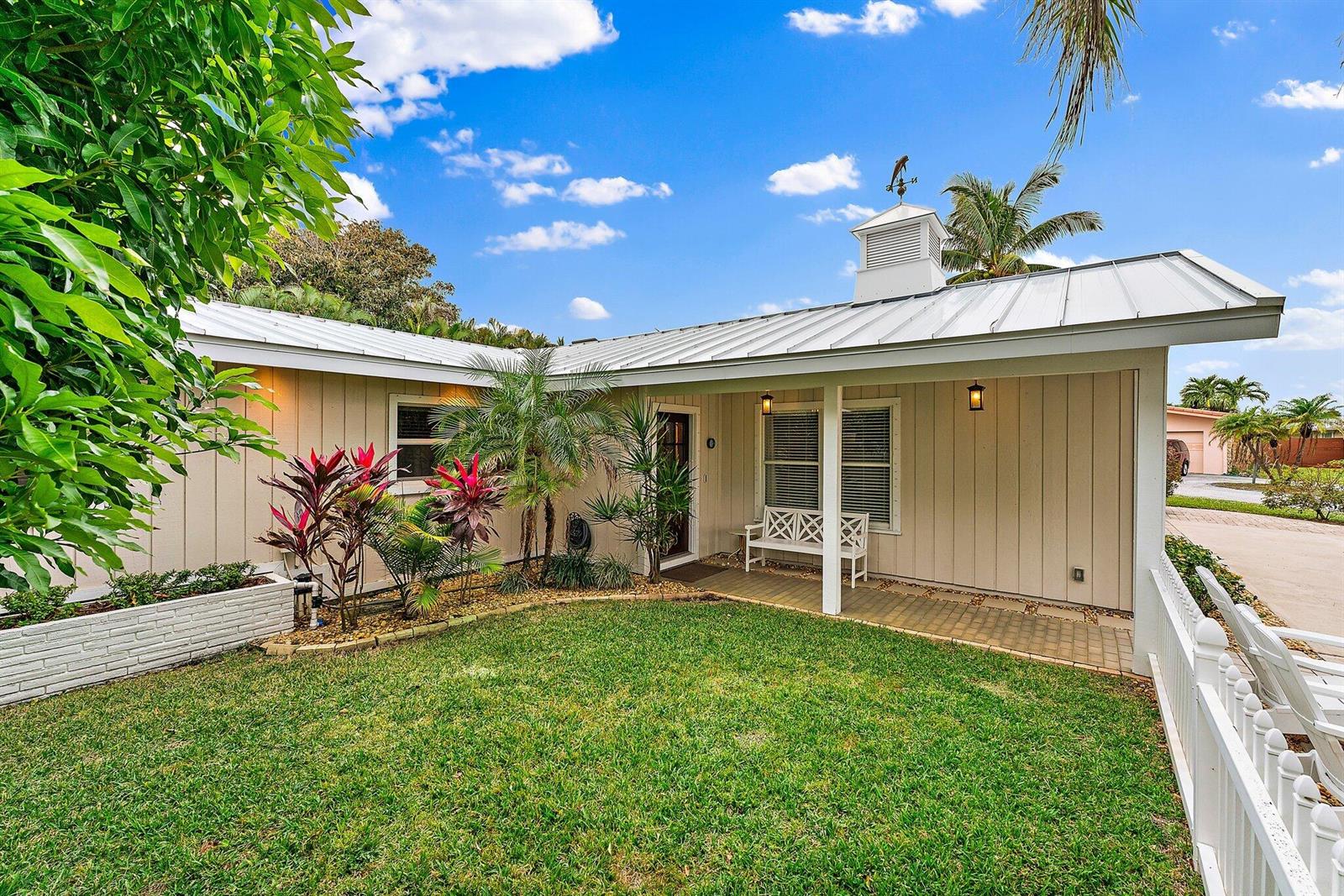 A single-story house with beige vertical siding, a metal roof, and a front porch — 460 Sunrise Way, Juno Beach FL 33408, JUNO BEACH, FL