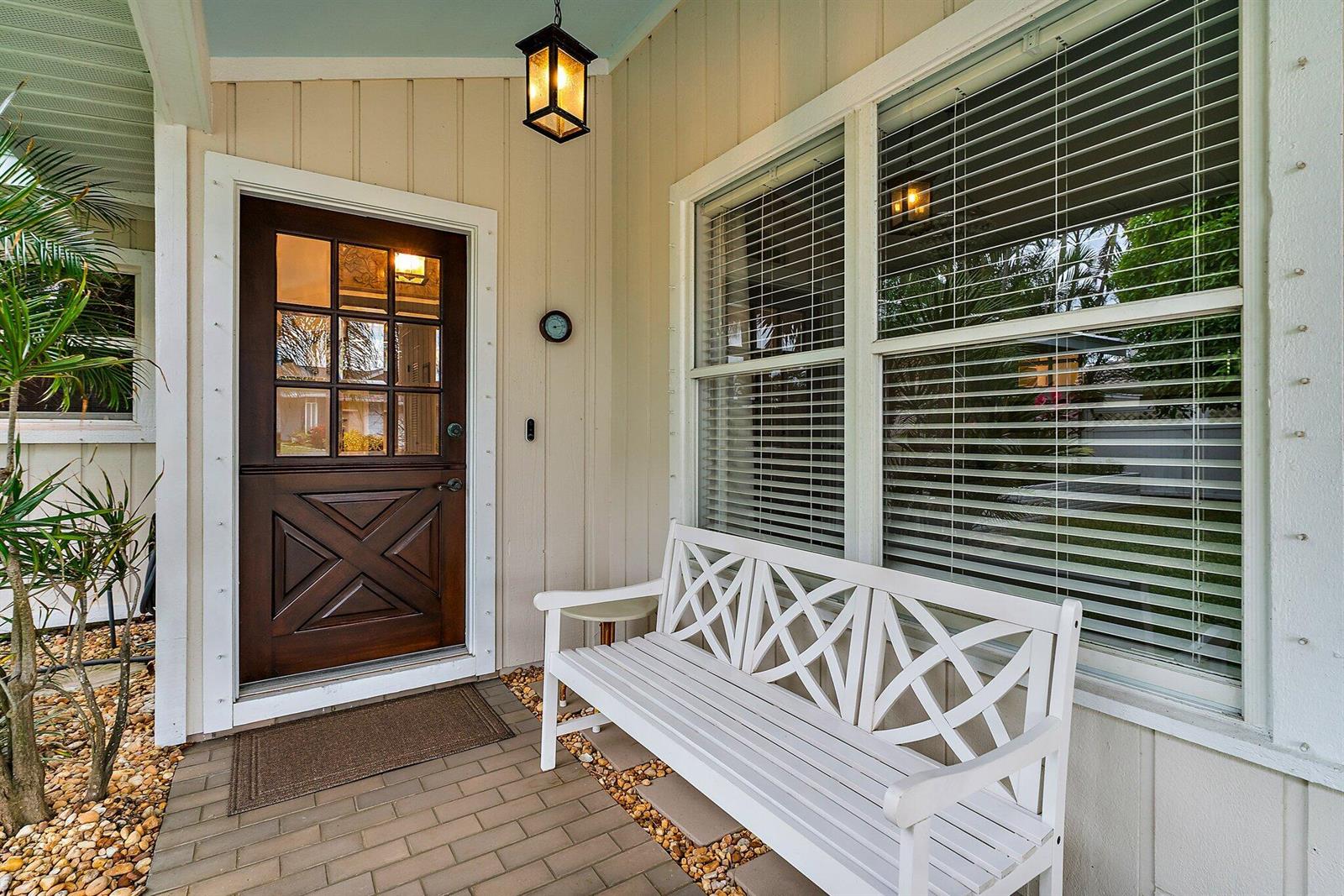 A front porch features a wooden door with glass panes, a white bench, and brick flooring — 460 Sunrise Way, Juno Beach FL 33408, JUNO BEACH, FL