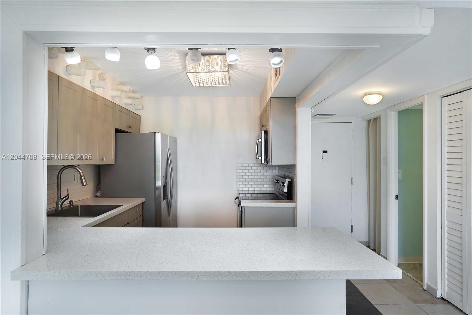 A kitchen features light wood cabinets, stainless steel appliances, and a white quartz breakfast bar — 6900 Bay Dr # 3H, Miami Beach FL 33141, MIAMI BEACH, FL