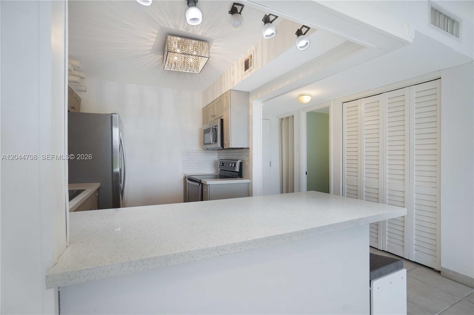 A kitchen features a white breakfast bar, stainless steel appliances, and a square crystal chandelier — 6900 Bay Dr # 3H, Miami Beach FL 33141, MIAMI BEACH, FL