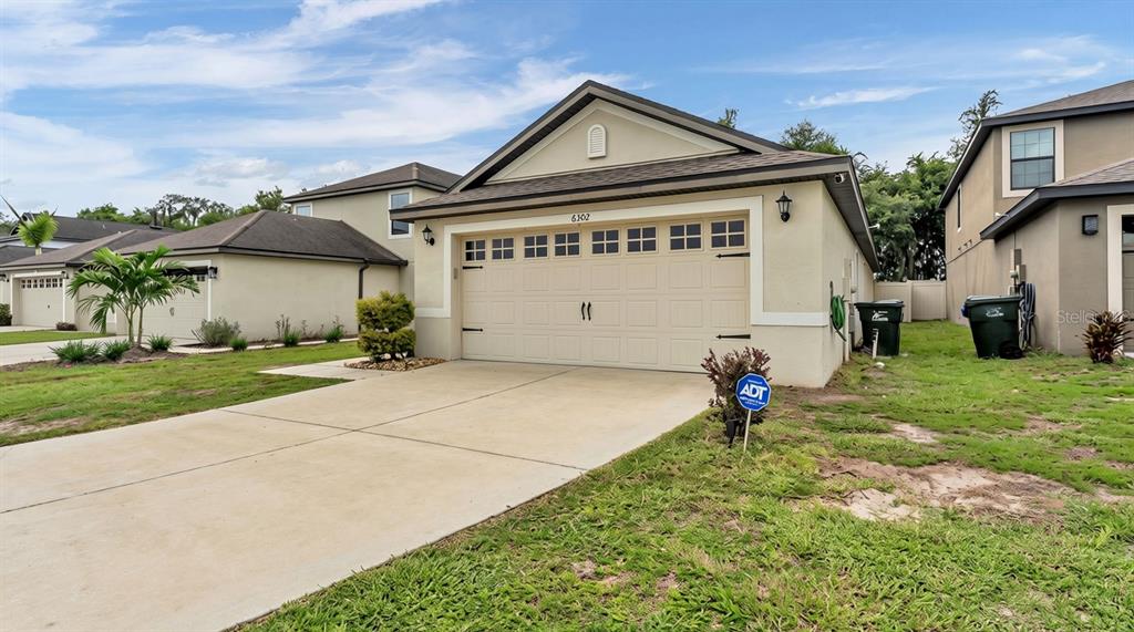 A tan single-story house with a two-car garage and a concrete driveway — 6302 MANITOBA DRIVE, LAKELAND, FL