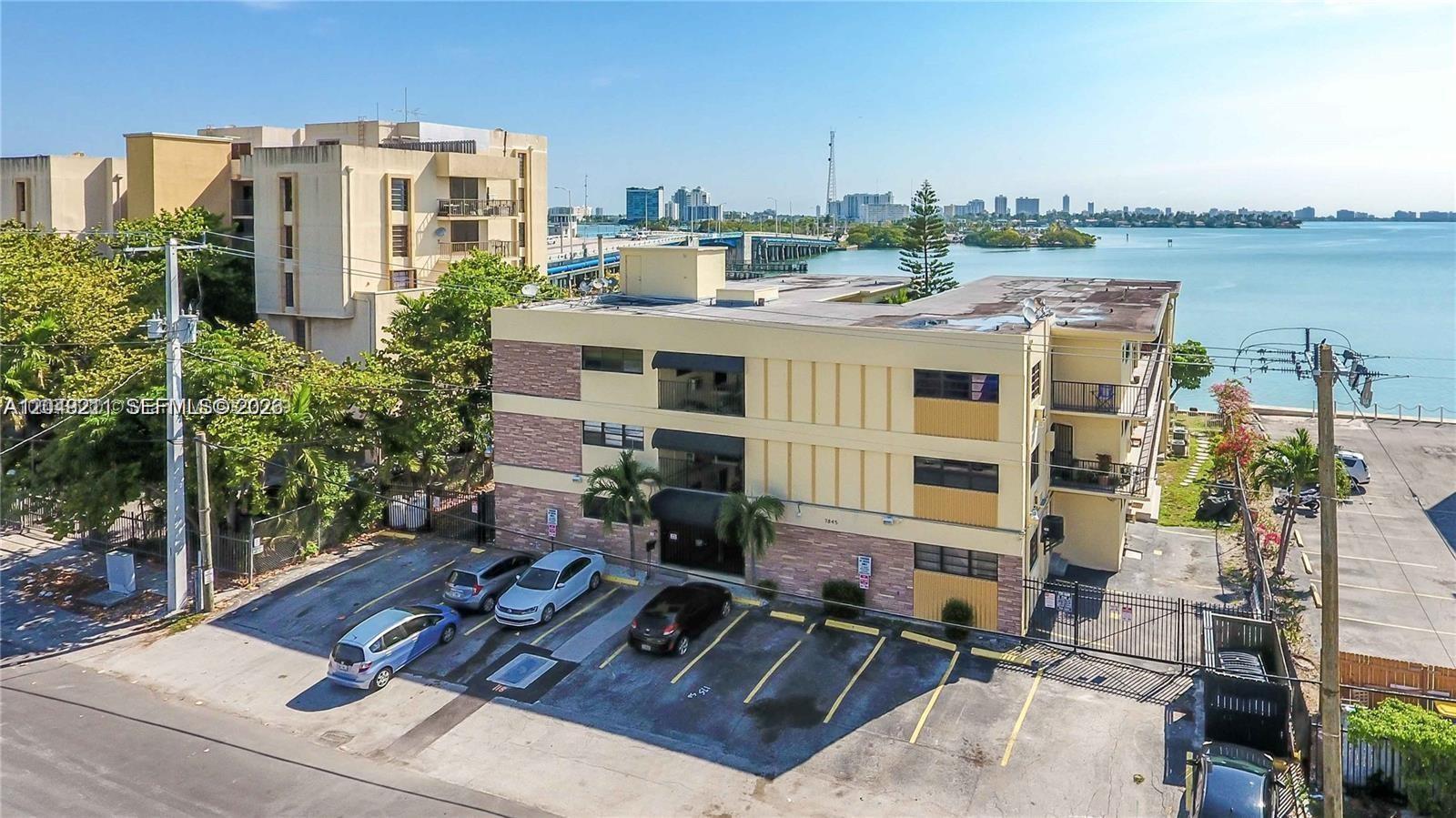 An aerial view shows a three-story apartment building with a parking lot and waterfront views — 7845 NE Bayshore Ct # 8, Miami FL 33138, MIAMI, FL