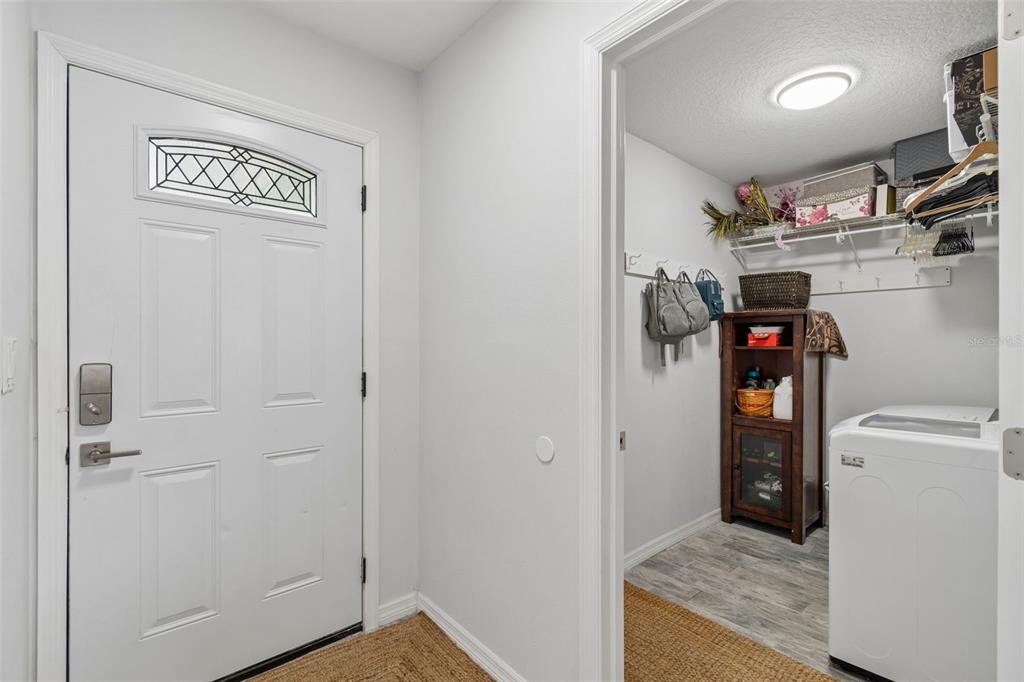 A white front door opens to a laundry room featuring a washer and storage shelving — 5440 LEAHY LANE, NEW PORT RICHEY, FL
