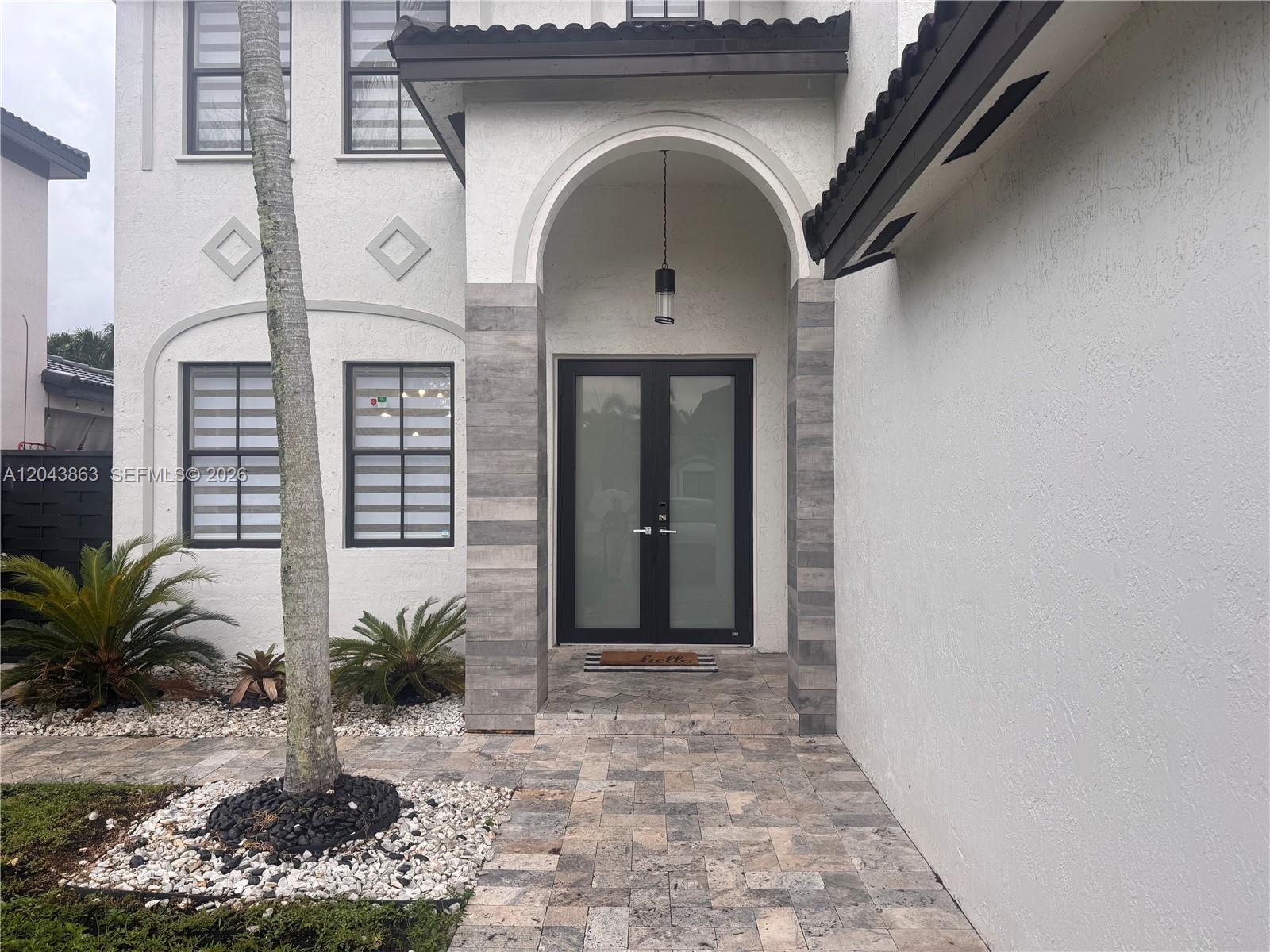The exterior of a white house features a stone-tiled entryway with double glass doors — 15376 SW 13th Ter, Miami FL 33194, MIAMI, FL