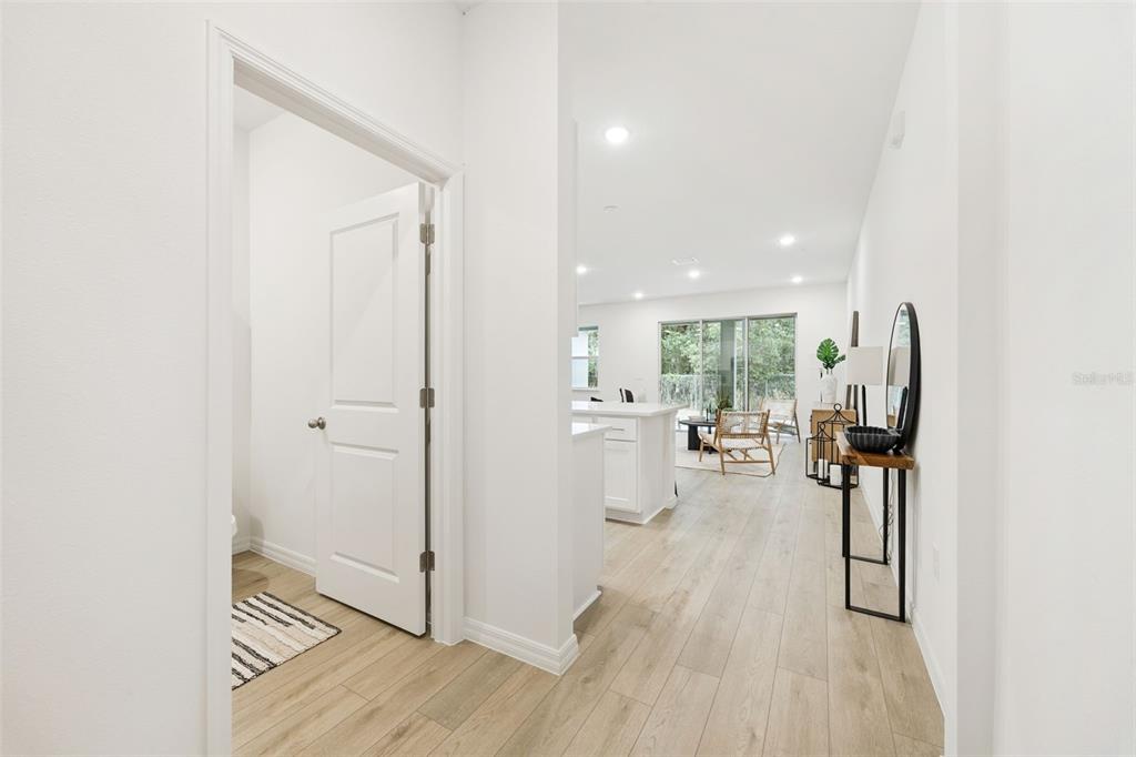 A hallway leads into a bright, open-concept kitchen and living area with light wood flooring — 5229 LUISA COURT, ST CLOUD, FL