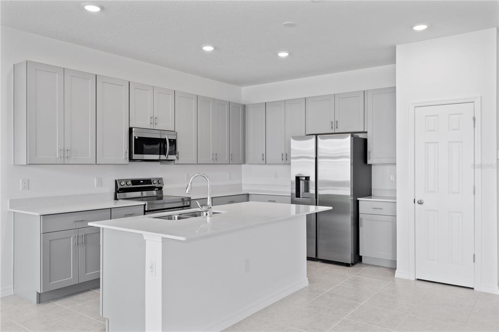 A modern kitchen features light gray cabinets, white countertops, a center island, and stainless steel appliances — 495 SILVER PALM DRIVE, HAINES CITY, FL