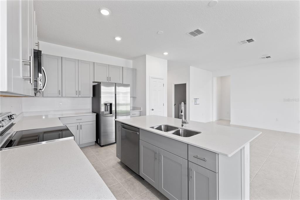 A modern kitchen features gray cabinets, white countertops, stainless steel appliances, and a central island — 495 SILVER PALM DRIVE, HAINES CITY, FL